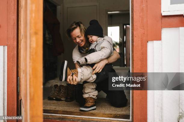 mother helping daughter wear boot seen through doorway - family getting dressed stock pictures, royalty-free photos & images