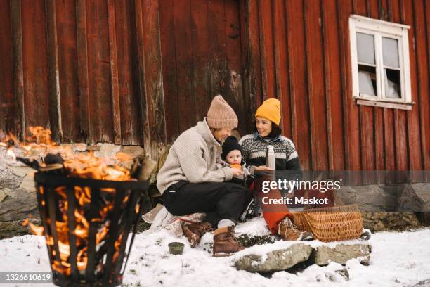 mature woman sitting with girlfriend feeding daughter against cottage during winter - place mat bildbanksfoton och bilder