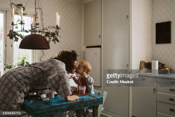 affectionate mother kissing daughter sitting at dining table in kitchen - västra götaland county stock pictures, royalty-free photos & images