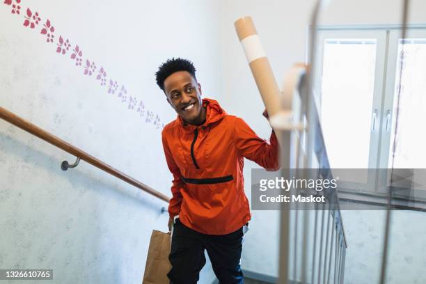 smiling young delivery person carrying courier while moving up on staircase - carrying bag stock pictures, royalty-free photos & images
