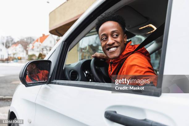 smiling young driver looking back through window while driving delivery van - van driver stock pictures, royalty-free photos & images