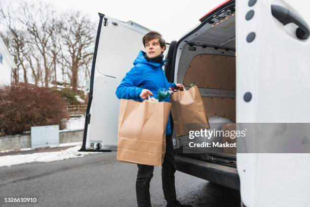 female delivery person unloading paper bags from van - livreur photos et images de collection