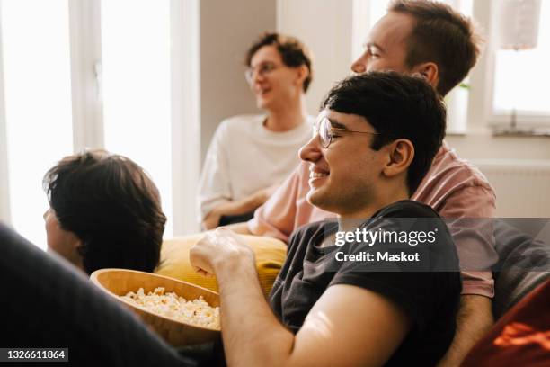 multi-ethnic male friends having popcorn while watching sports in living room - manly room stock pictures, royalty-free photos & images