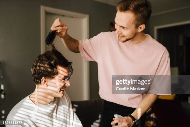 young man combing male friend's hair while sitting at home - hair brush stock pictures, royalty-free photos & images