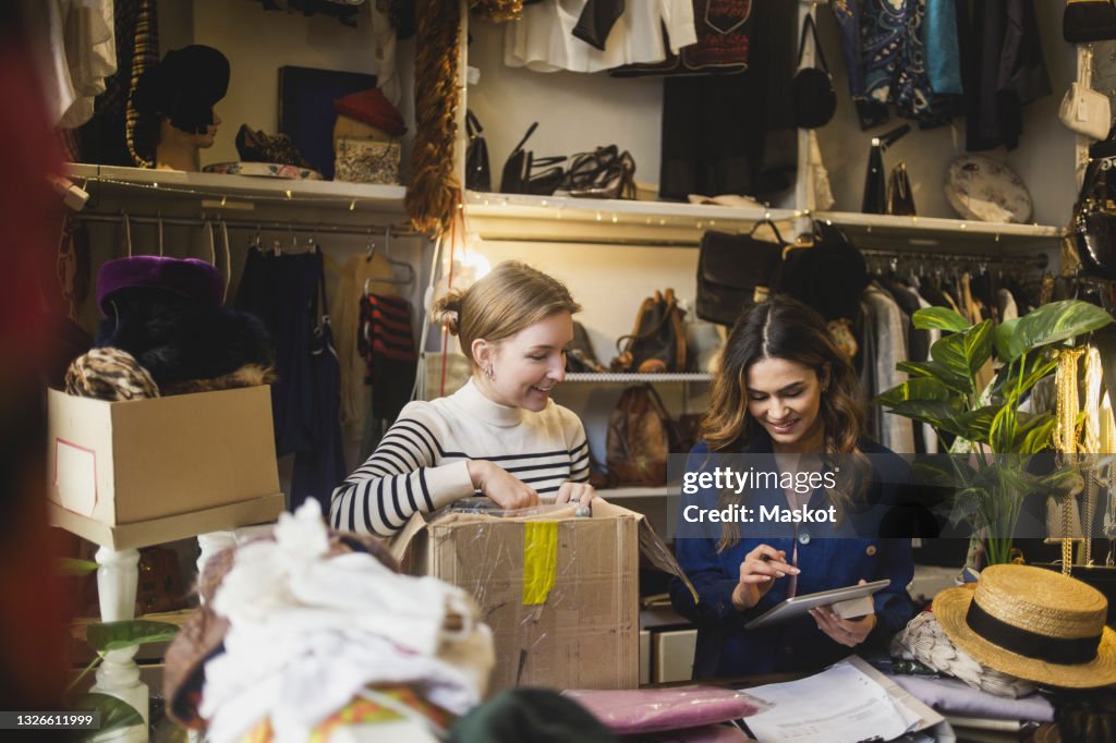 Smiling owner using digital tablet standing by female colleague in boutique