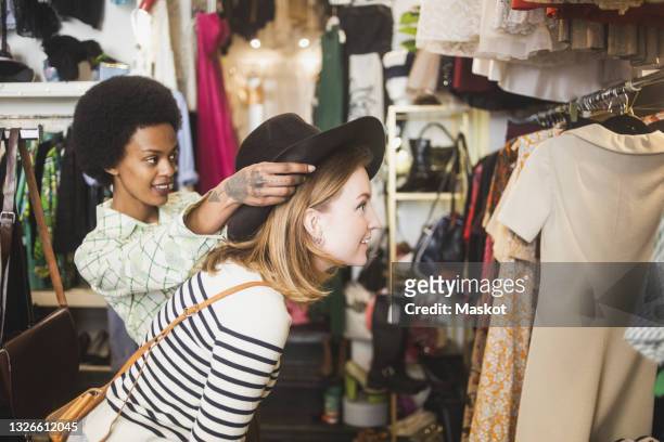 store owner trying hat on female customer in boutique - green hat fotografías e imágenes de stock