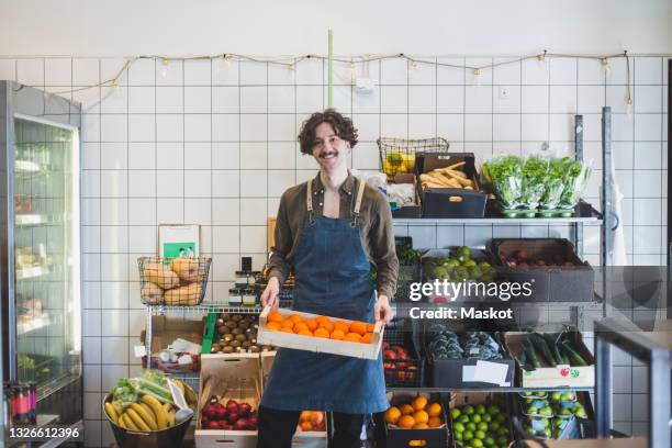 portrait of smiling male owner with fruit box in store - delicatessen stock pictures, royalty-free photos & images