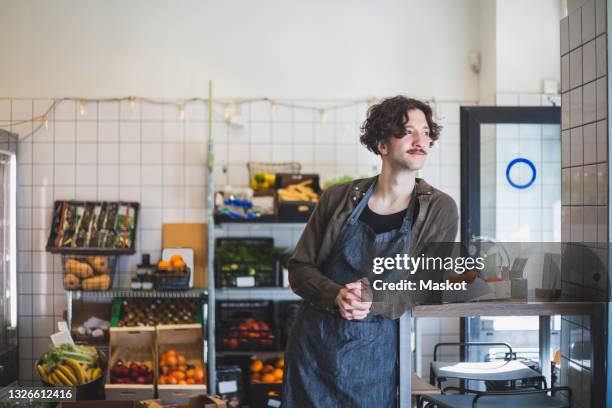 male owner looking away while leaning on table at store - table of content stock pictures, royalty-free photos & images