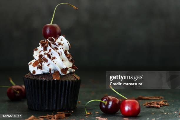 bild von einzelnen, hausgemachte, schwarzwald gateau cupcake in braunem papier kuchen fall, gerohrte schlagsahne rosette gekrönt mit morello kirsche mit schokoladenspänen bestreut, schwarzer hintergrund, fokus auf den vordergrund - kuchen dekorieren stock-fotos und bilder