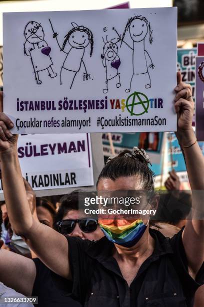 Demonstrator wearing a rainbow face mask holds up a placard reading 'The Istanbul Convention keeps you alive' during a protest against the Turkish...