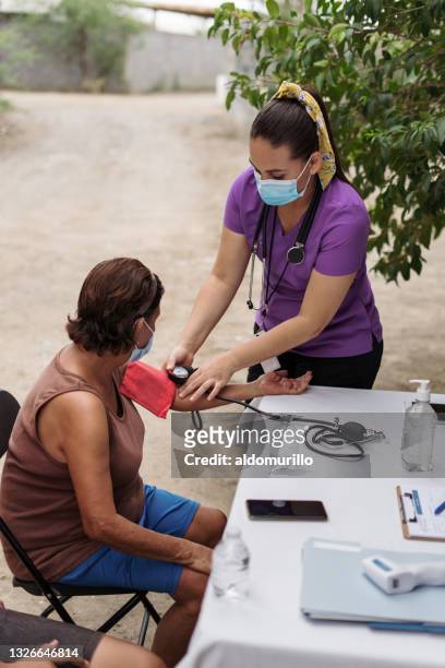 enfermera con mascarilla y controlando la presión arterial al aire libre - flu mask in mexico fotografías e imágenes de stock