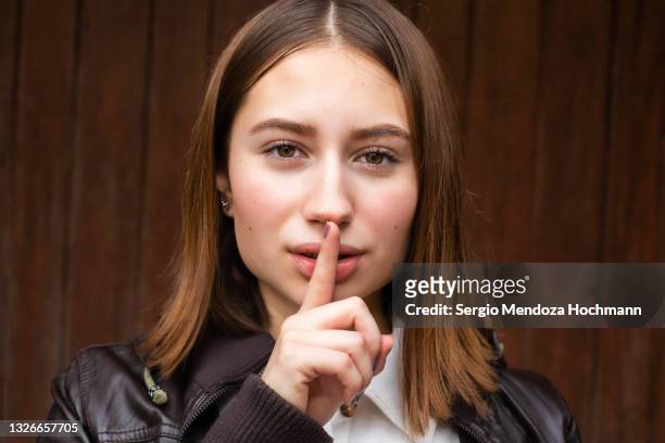 young mexican woman looking at the camera with a finger on her lips, asking for quiet, silence - be silent stock-fotos und bilder