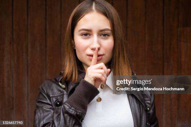 young mexican woman looking at the camera with a finger on her lips, asking for quiet, silence - be silent stock-fotos und bilder