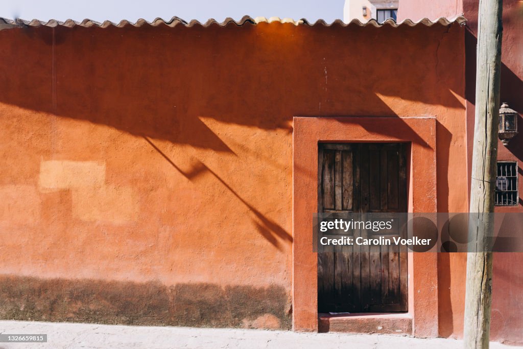 Humble colonial-style house with wooden door surrounded by orange wall in San Miguel de Allende