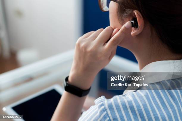 a young southeast asian woman in casual attire is using a wireless earphones - in ear headphones stock-fotos und bilder