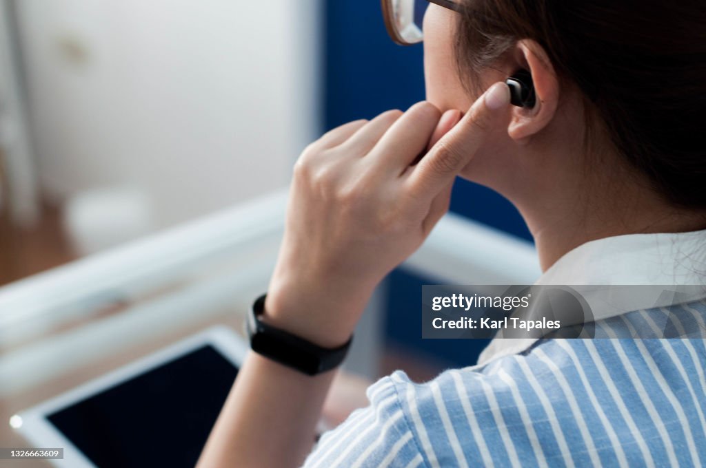 A young Southeast Asian woman in casual attire is using a wireless earphones