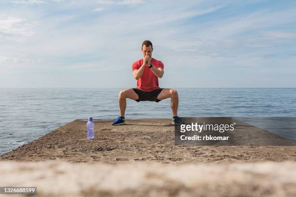 young man doing wide squatting on the beach - beach bum imagens e fotografias de stock