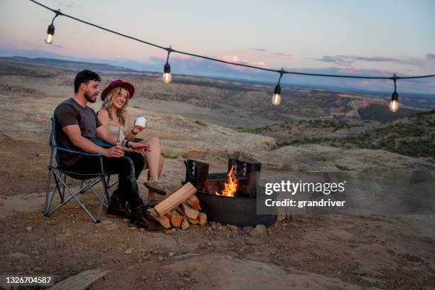 young happy couple sitting by a warm inviting campfire enjoying the van life at a desert campsite at dusk - desert camping stock pictures, royalty-free photos & images