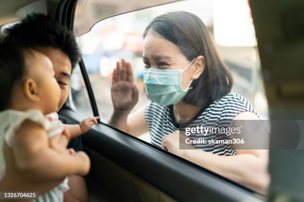 asian mother wearing protective face mask and say hi baby daughter(2-5month)and teenager son inside the car  protecting covid-19 spread - family inside car fotografías e imágenes de stock