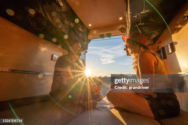 couple talking and relaxing, sitting cross legged in their camper van as the sun is setting - surprised woman looking at tablet stock pictures, royalty-free photos & images