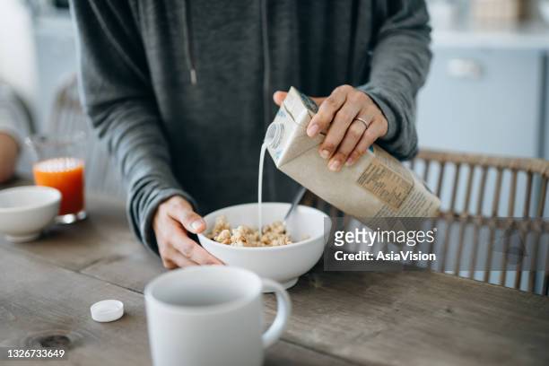 cropped shot of young asian mother preparing healthy breakfast, pouring milk over cereals on the kitchen counter. healthy eating lifestyle - pouring stock pictures, royalty-free photos & images