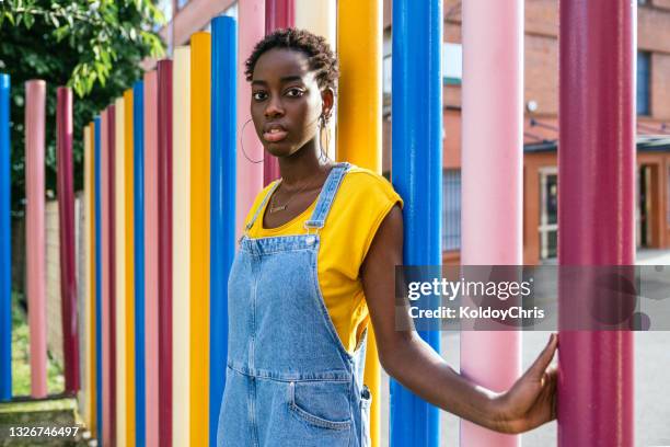 side view of young african-american woman against coloful poles behind - jeans latzhose frau stock-fotos und bilder