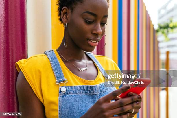 close-up of young woman using phone with a colorful background in a sunny day - leuchtende farbe stock-fotos und bilder