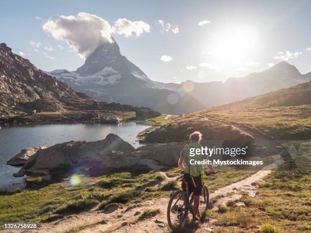 male mountain biker pauses to look at the matterhorn mountain - monte cervino stockfoto's en -beelden