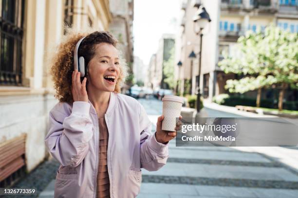 porträt eines glücklichen mädchens, das unterwegs musik genießt und kaffee trinkt - in ear headphones stock-fotos und bilder