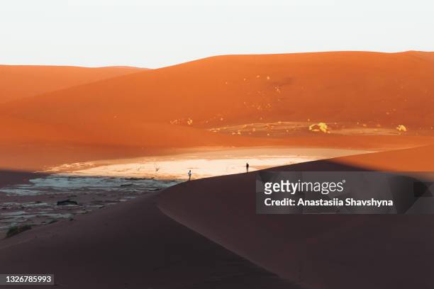 woman and man traveler exploring dramatic desert landscape with sand dunes during sunrise at sossuvlei, namibia - sossusvlei stock pictures, royalty-free photos & images