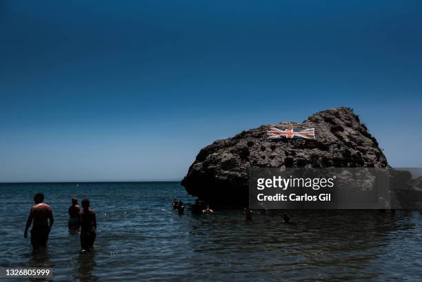 Several people take a bath in the sea next to a rock that has a flag of the United Kingdom, in the Catalan Bay, one of the most famous beaches in...