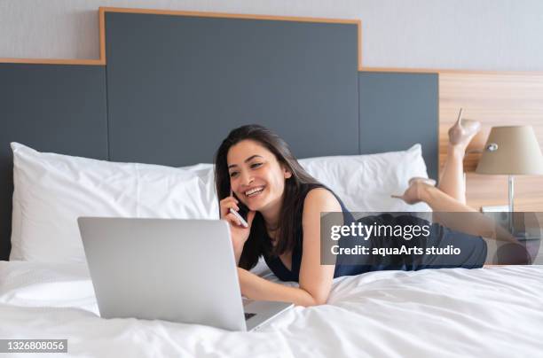 businesswoman lying on bed and working on laptop while using smartphone i̇n hotel room - woman smiling facing down stock pictures, royalty-free photos & images