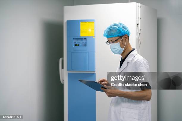 asian male researcher using tablet in front of medical refrigerator - cold storage room stock pictures, royalty-free photos & images