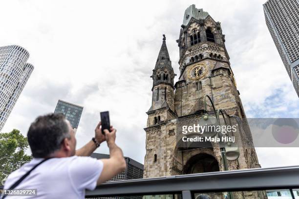 Tourist takes a photo of the Kaiser Wilhelm Memorial Church as he rides a double-decker tourist bus on July 03, 2021 in Berlin, Germany. Tourism is...
