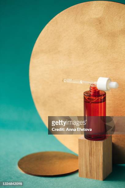red glass bottle with pipette on it and with essential oil or moisturizing lotion on wooden podium near golden timber circles on table and on teal blue background. concept of organic cosmetics and natural components. front view with copy space for your de - cbd products stock pictures, royalty-free photos & images