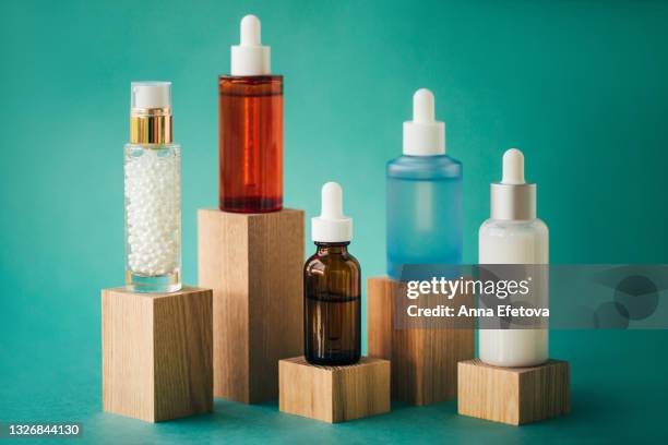 set of many various vials with organic essential oils or face serums on wooden podiums on teal blue background. bottles made of red, matte turquoise, transparent, white and amber glass. concept of natural cosmetics. front view with copy space - cosmetic bottle stockfoto's en -beelden