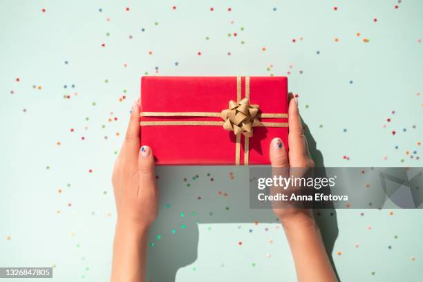 hands are holding red gift box with glittering gold bow on pastel light blue background with many star shaped confetti. flat lay style - confetti light blue background stock pictures, royalty-free photos & images