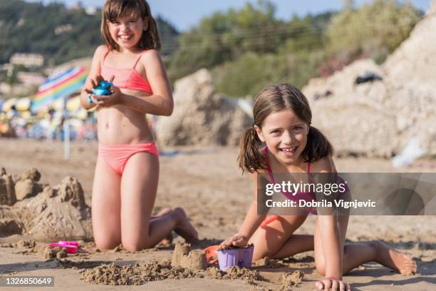 enfants heureux façonnant une forme de sable à la plage - fille maillot photos et images de collection