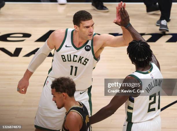 Trae Young of the Atlanta Hawks hangs his head as Brook Lopez and Jrue Holiday of the Milwaukee Bucks celebrate a series win against the Atlanta...