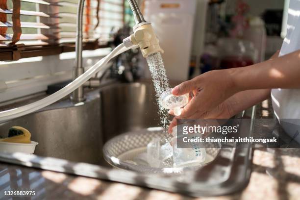 close up of hand mother washing baby bottle in kitchen sink at home. - bébé biberon photos et images de collection