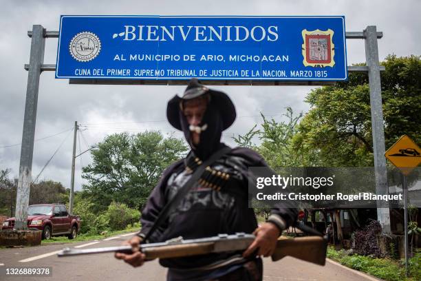 An armed member of Pueblos Unidos poses in front of the Welcome to the municipality of Ario de Rosales sign on July 4, 2021 in Ario de Rosales,...