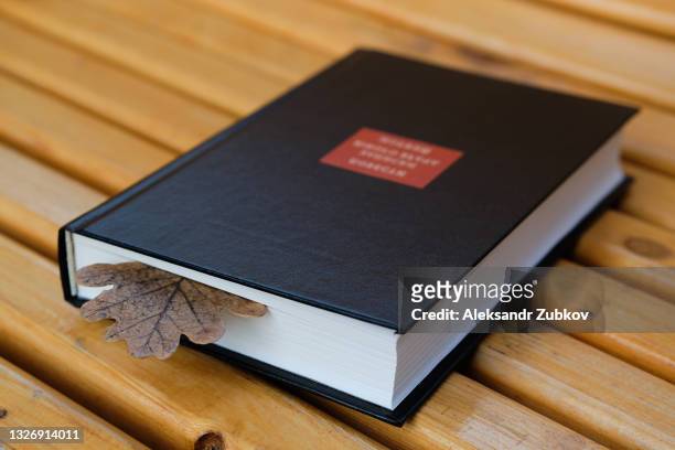 a colorful autumn oak leaf is laid between the pages of a closed book. textbook or fiction on a wooden bench in the park, on an autumn day. - romance book covers stock pictures, royalty-free photos & images
