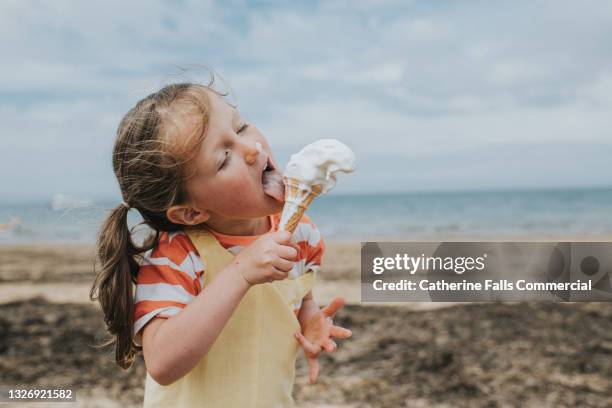 a little girl stands on a beach and eats a melting ice-cream - polo fotografías e imágenes de stock