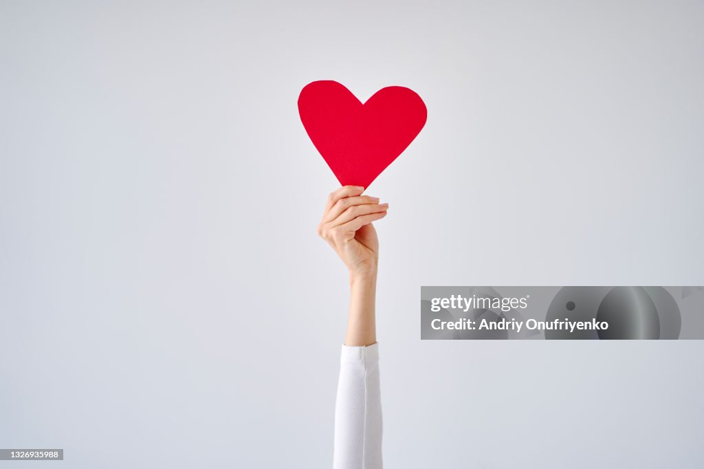 Female's hand holding red heart against white grey background.