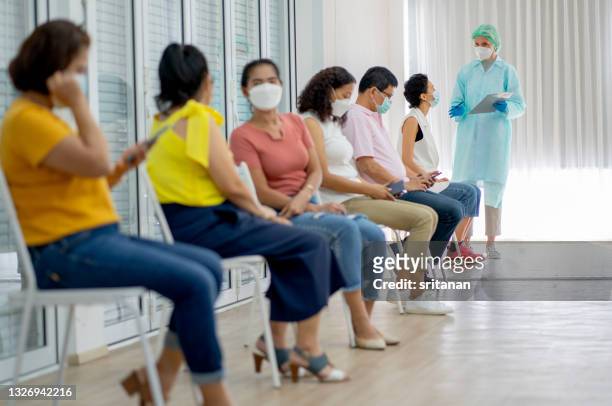 group of people sit on chair in one role waiting for covid-19 vaccination and medical staff with green uniform hold document chart for checking - medical research group stock pictures, royalty-free photos & images