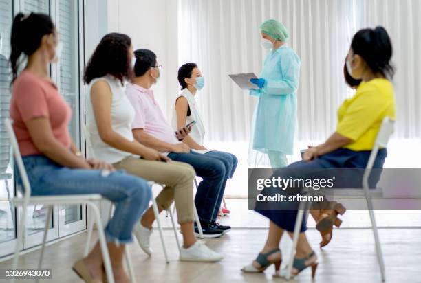 group of people sit on chair in two roles waiting for covid-19 vaccination and medical staff with green uniform hold document chart - court case stock pictures, royalty-free photos & images