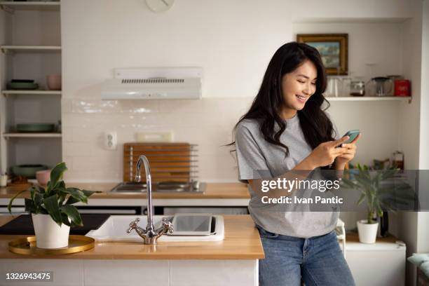 beautiful young woman of mongolian ethnicity using a smart phone at home - bel appartement stockfoto's en -beelden