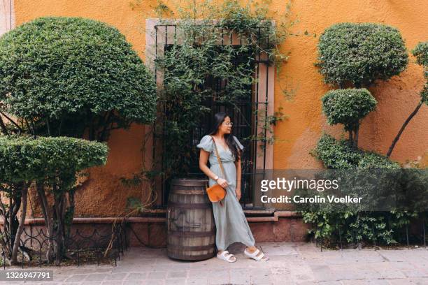 woman in maxi dress standing in front of yellow wall with plants - long dress stock-fotos und bilder