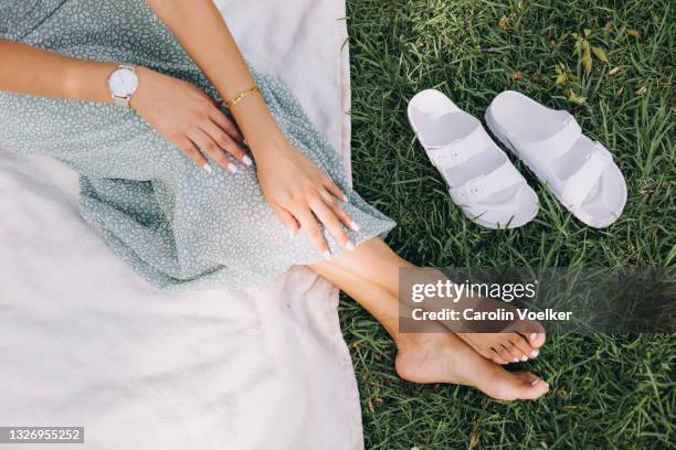 hand and feet of a woman wearing a maxi dress on a picnic blanket in nature - groene schoen stockfoto's en -beelden