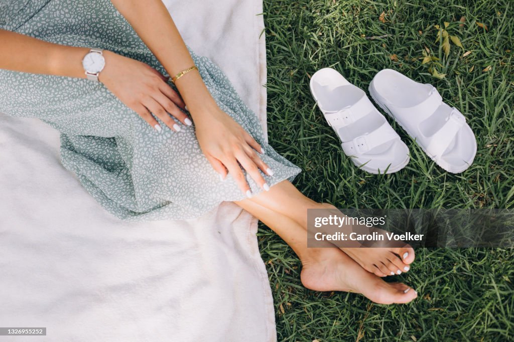Hand and feet of a woman wearing a maxi dress on a picnic blanket in nature